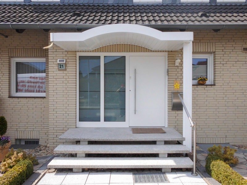weißes geschwungenes Vordach über einen weißen Haustür ans einem Privathaus im Bungalowstil